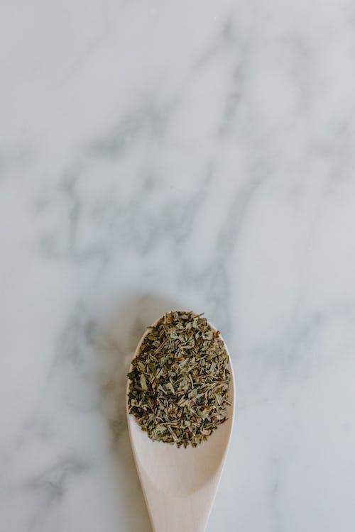 Free Top view of dried leaves of green tea in spoon placed on white marble surface in bright room Stock Photo